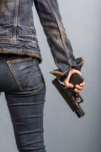 Midsection of woman holding handgun while standing by wall