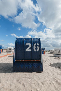 Hooded beach chairs on sand against sky