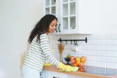 African-american woman in rubber gloves occupied with household duties in kitchen