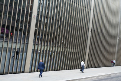 Rear view of people walking on sidewalk by building