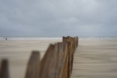 Wooden railing at beach against cloudy sky