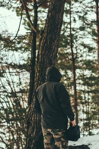 Rear view of man standing by tree trunk in forest