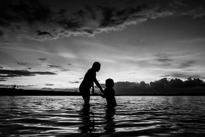 Silhouette of friends on water against sky during sunset