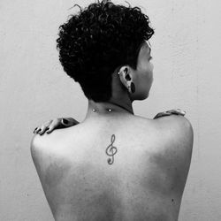 Rear view of shirtless woman with tattoo and piercing on back by wall