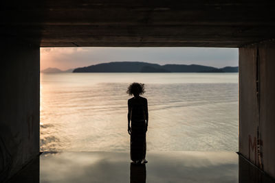 Rear view of man standing by sea against sky