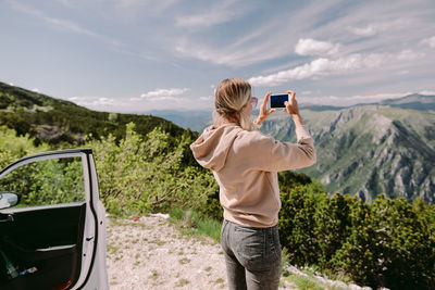 Man photographing with mobile phone against sky