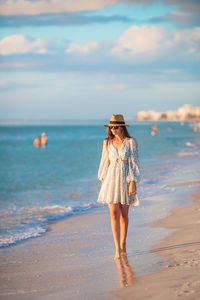 Rear view of woman standing at beach against sky