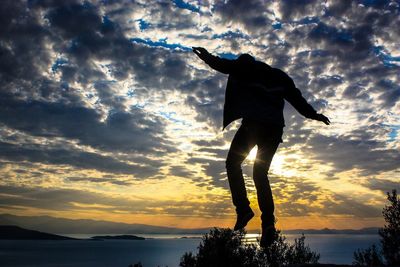 Silhouette of woman standing on beach against cloudy sky at sunset