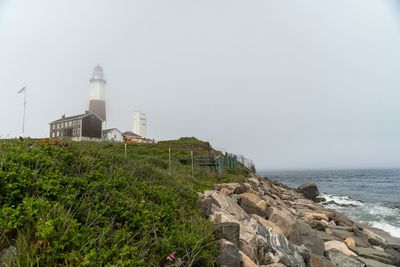 Lighthouse amidst sea and buildings against clear sky
