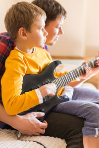 Father with son playing guitar while relaxing at home