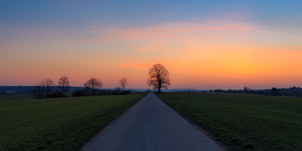 Road amidst field against sky during sunset