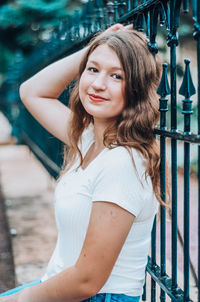 Portrait of smiling teenager sitting by railing outdoors