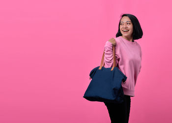 Young woman standing against pink background
