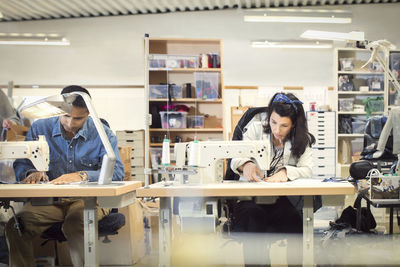 Serious man and woman sewing clothes at workshop