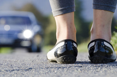 Low section of woman standing on road with car in background