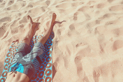Low section of man resting on patterned towel at beach