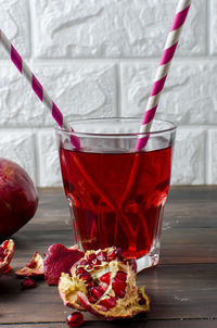 Close-up of juice by pomegranate in glass against wall on table