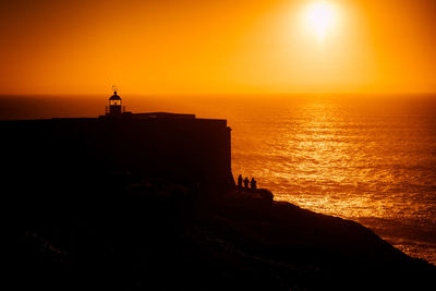 Silhouette built structure by sea against orange sky