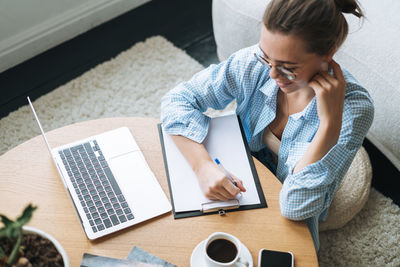 Side view of young woman using laptop while sitting on table