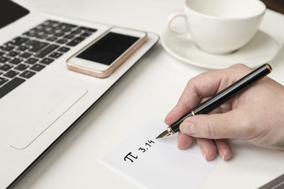 Close-up of hand holding coffee cup on table