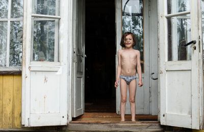 Portrait of shirtless man standing against door