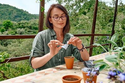 Woman sowing medicinal or aromatic herbs in clay pot on balcony. home planting and food growing.