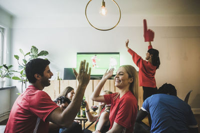 Smiling man and woman high-fiving while celebrating victory with friends at home