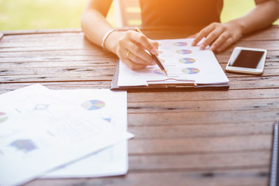 Cropped hands of woman analyzing graphs by mobile phone on table