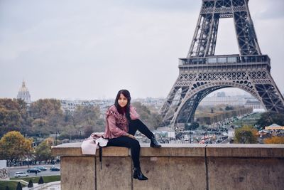 Portrait of young woman sitting against eiffel tower