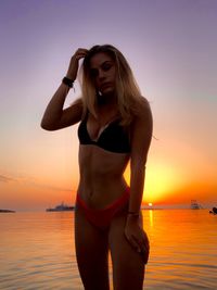 Young woman standing by sea against sky during sunset