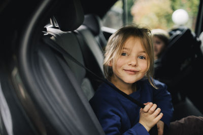 Portrait of smiling girl holding seat belt while sitting in car