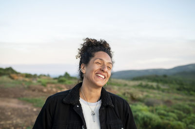 Woman smiling while standing outdoors in nature.