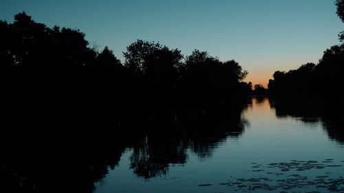 Silhouette trees by lake against sky during sunset