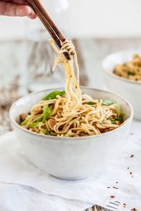 Cropped hand of woman eating noodles with chopsticks in bowl on table