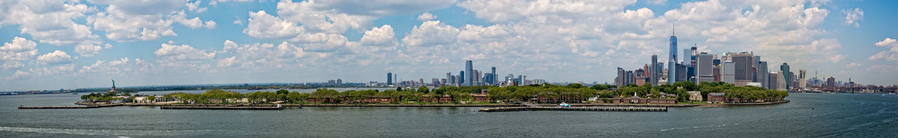 Panoramic shot of city by river against cloudy sky