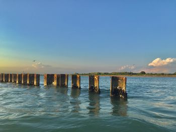 Wooden posts in sea against sky