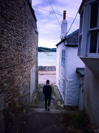 Rear view of man walking on alley amidst buildings in city