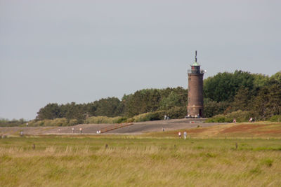 Lighthouse on field by building against sky