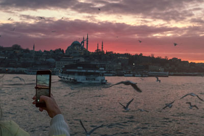 Man photographing by cityscape against sky during sunset