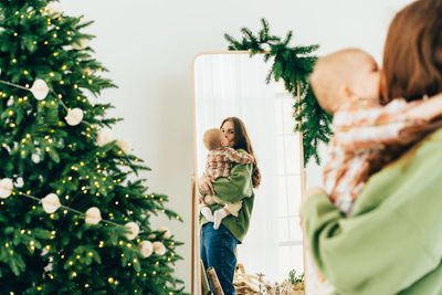 Attractive caucasian redhead mother holding her baby and looking in the mirror on christmas day. 