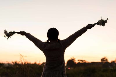 Rear view of silhouette person standing on field against sky during sunset