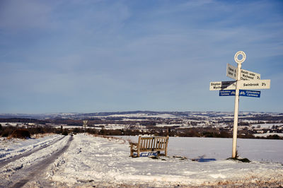 Road sign on snow covered landscape against sky