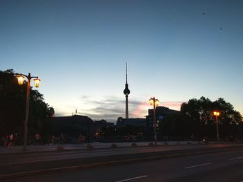 Illuminated street lights on road against fernsehturm in city at dusk