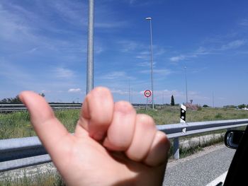 Cropped hand showing thumbs up against blue sky