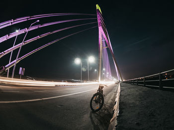 Light trails on bridge over road against sky at night