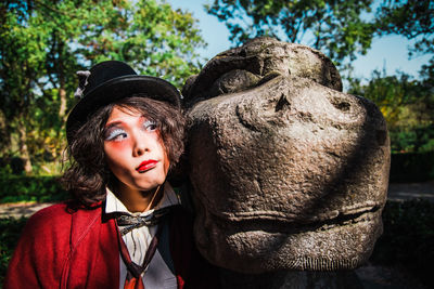 Portrait of young man cosplaying mad hatter with statue against trees