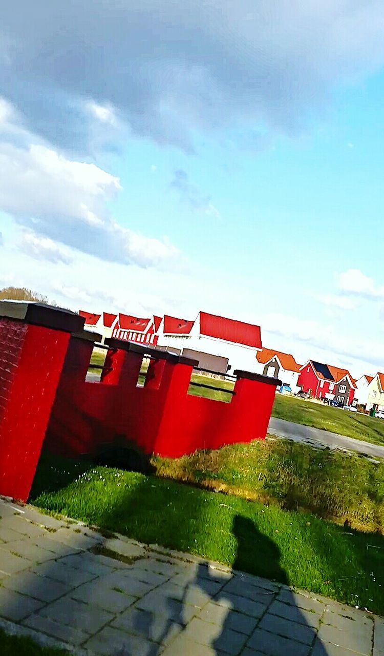 sky, built structure, building exterior, architecture, cloud - sky, red, empty, outdoors, chair, day, sunlight, cobblestone, grass, cloud, bench, footpath, absence, cloudy, no people, roof