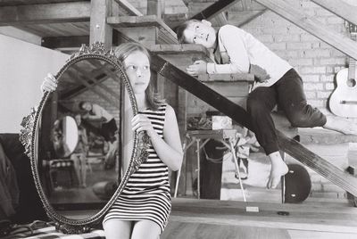 Girl holding mirror while boy relaxing on staircase at home