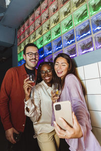 Cheerful woman taking selfie with male and female friends through smart phone in bar