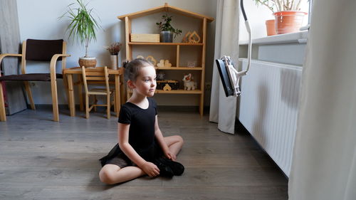 Boy looking away while sitting on wooden floor at home